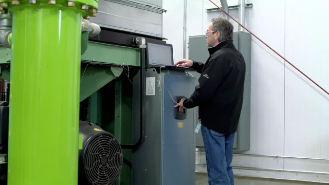 Technician using a laptop beside an industrial compressor control panel