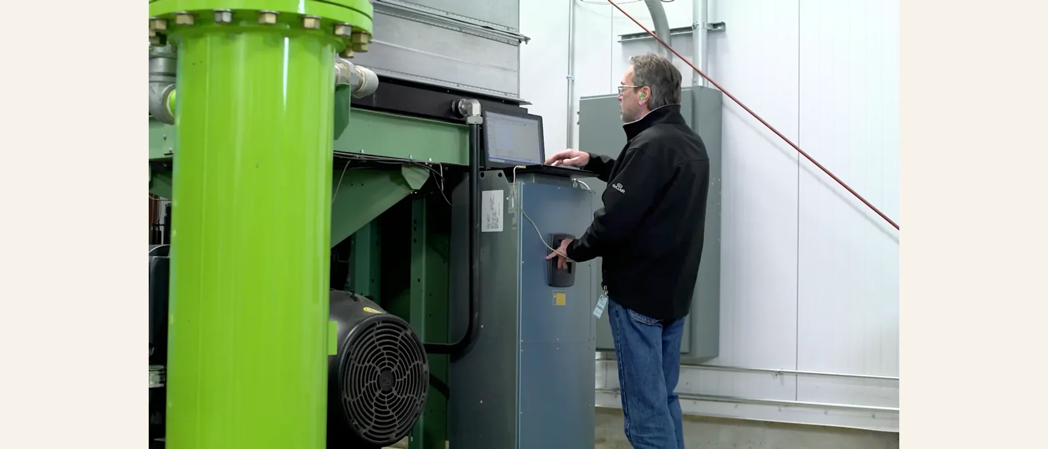 Technician using a laptop beside an industrial compressor control panel