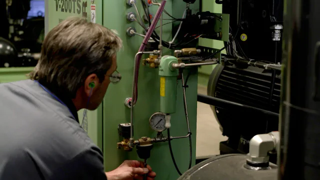 Technician maintaining a compressor drain valve inside a green machine enclosure