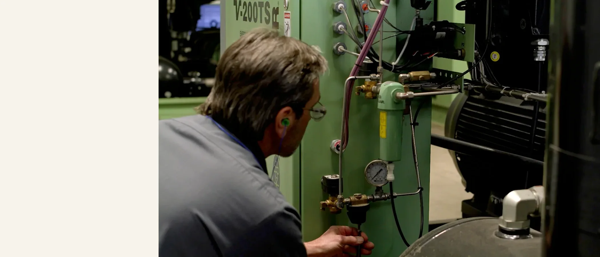 Technician maintaining a compressor drain valve inside a green machine enclosure