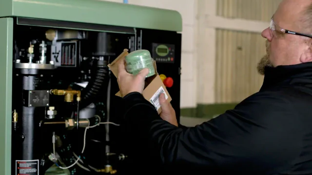 Technician inspecting a compressor oil filter inside a green machine