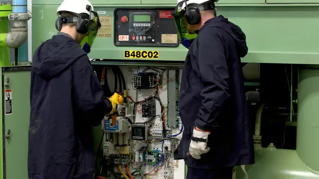 Two technicians in safety gear servicing a large industrial compressor