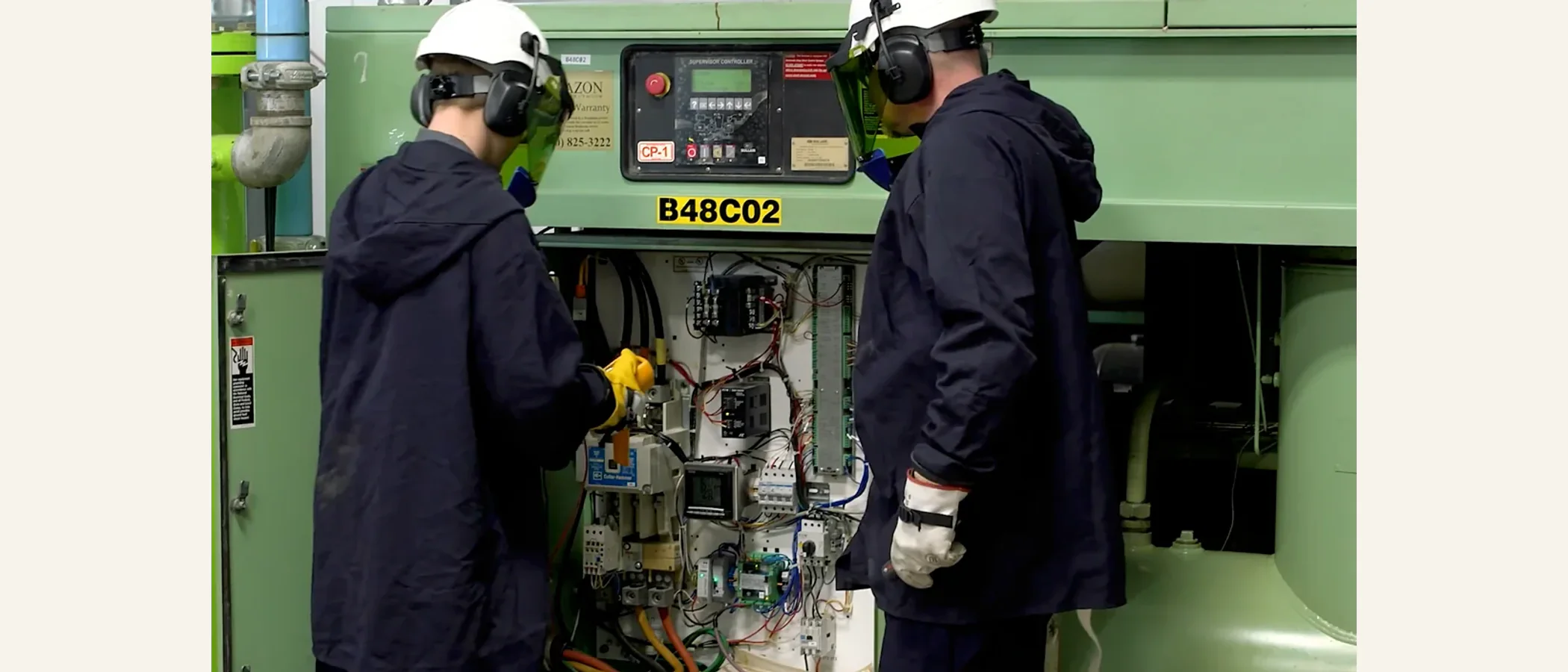 Two technicians in safety gear servicing a large industrial compressor